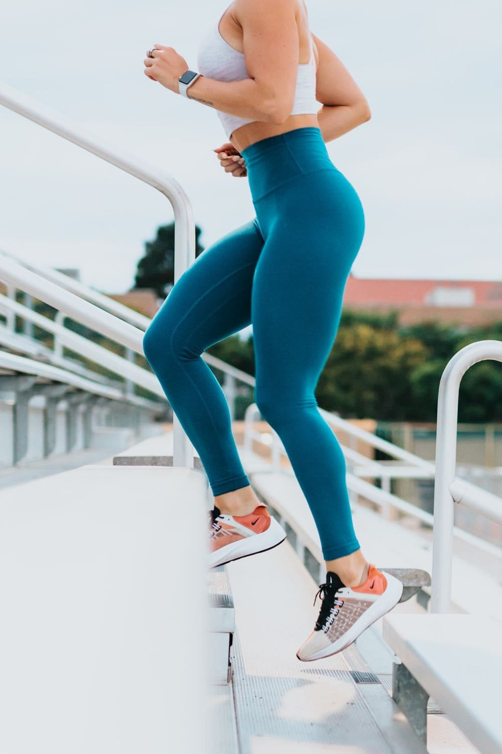 woman in blue leggings running up bleachers