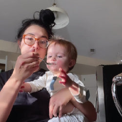A woman wearing glasses feeds oatmeal to a baby with a spoon.